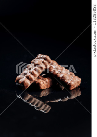 Crunchy chocolate bars with nuts on dark background, ideal for snacks and dessert presentations Crunchy chocolate bars with nuts on dark background, ideal for snacks and dessert presentations 118289858