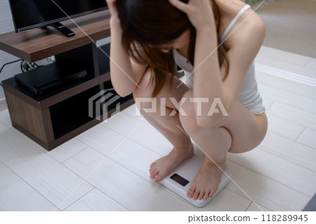 Woman weighing herself in underwear, holding her head, regretting, worrying about her weight 118289945