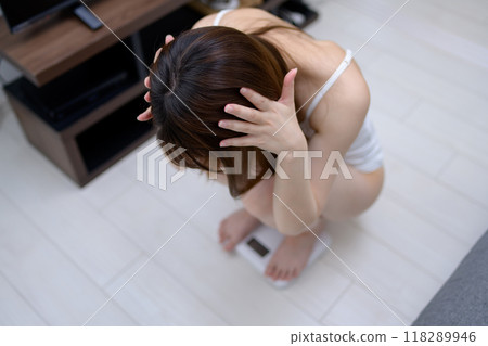 Woman weighing herself in underwear, holding her head, regretting, worrying about her weight 118289946