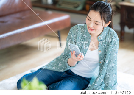 A young woman relaxing in the living room while looking at her smartphone A young woman relaxing in the living room while looking at her smartphone 118292140