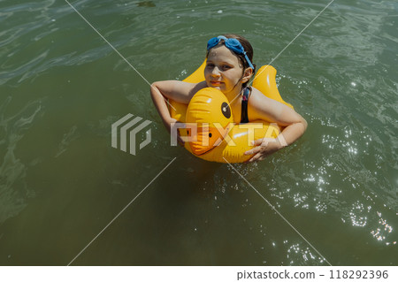 Girl floating in the lake with inflatable yellow duck on a sunny day. Young girl playing with inflatable yellow duck in the water on a sunny day 118292396