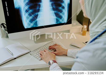 Medical professional analyzing chest x-ray on computer in modern office environment with minimal decor and professional equipment visible on desk Medical professional analyzing chest x-ray on computer in modern office environment with minimal decor and professional equipment visible on desk 118293134
