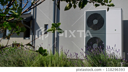 Outdoor heat pump unit with lavender plants in a modern garden setting, with a house in the background. Outdoor heat pump unit with lavender plants in a modern garden setting, with a house in the background. 118296393
