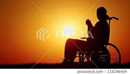 Silhouette of a person in a wheelchair during a sunset, reflecting in a peaceful moment. 118296404