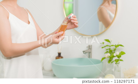 Serum advertising pic with bathroom concept and female model, the model on the left side of photo is opening an unbranded clear serum bottle, which contains yellow essence 118297171