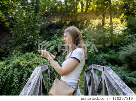 A female blogger takes photos and videos in a botanical garden, a beautiful park in nature. She holds a telescopic tripod monopod with a smartphone 118297519