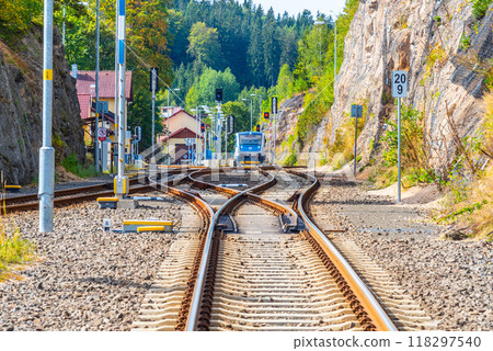 The railway tracks curve through Smrzovka station in Czechia, showing a train approaching in bright daylight. Surrounding greenery and buildings add to the picturesque setting. The railway tracks curve through Smrzovka station in Czechia, showing a train approaching in bright daylight. Surrounding greenery and buildings add to the picturesque setting. 118297540