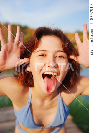 Funny young woman in a blue swimsuit with her tongue sticking out.  118297919