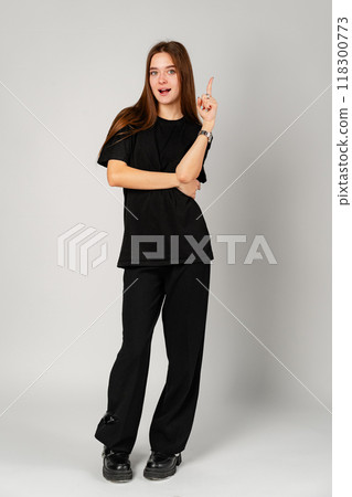 Smiling Young Woman Pointing to Copy Space Against a Grey Background 118300773