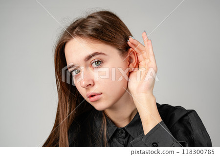 Young Woman in Black Shirt Listening Intently Against a Neutral Background. 118300785