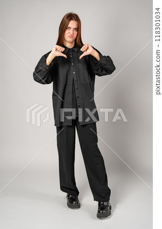 Young Woman Giving Thumbs Down Gesture Against a Gray Background 118301034
