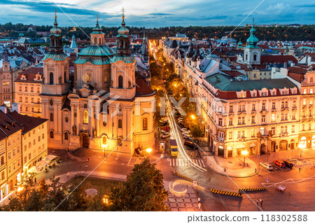 St Nicholas Cathedral stands illuminated against the evening sky in Prague's Old Town. The charming streets and architecture surround the cathedral, creating a picturesque atmosphere. 118302588