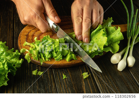 A chef uses a knife on a cutting board to cut lettuce leaves to prepare a vegetable dish for breakfast 118302656