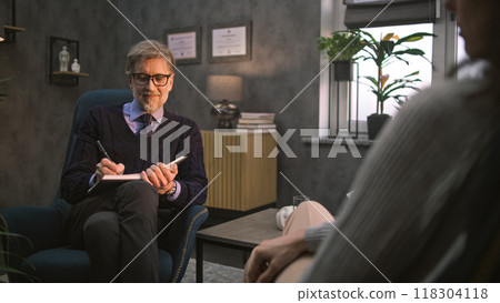 Mature psychotherapist takes notes, listens to patient, asks questions during therapy 118304118