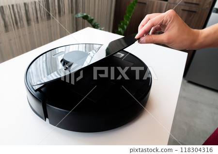 Modern robot vacuum cleaner after cleaning the apartment, a woman's hand opens the container lid to clean the vacuum cleaner after cleaning 118304316