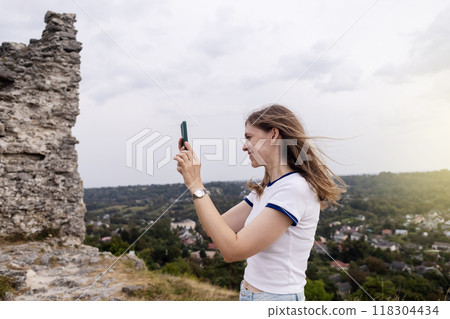 A young woman takes a photo on her phone of a beautiful view of the city from the top of the mountain. Photos and videos on a smartphone. Travel blogger and influencer 118304434