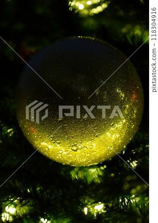 Large golden glittery ball hanging on Christmas tree in the dark, illuminated from below like a moon. Vertical template for a minimalist Christmas card. Close-up, blurred background. Large golden glittery ball hanging on Christmas tree in the dark, illuminated from below like a moon. Vertical template for a minimalist Christmas card. Close-up, blurred background. 118304916