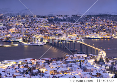Panorama of Norwegian city of Troms in the winter. Snowy roofs, bridge, embankment near the port and fishing ships. Evening lights Panorama of Norwegian city of Troms in the winter. Snowy roofs, bridge, embankment near the port and fishing ships. Evening lights 118305282