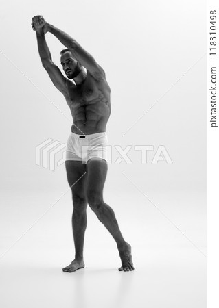 Dynamic shot of man's side profile, with his arm stretched out and muscles flexed. Intense gaze and sculpted body. Black and white photo. Dynamic shot of man's side profile, with his arm stretched out and muscles flexed. Intense gaze and sculpted body. Black and white photo. 118310498