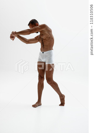 Man stands tall, reaching forward as his body twists slightly. His toned abs and strong legs accentuated against white background. Man stands tall, reaching forward as his body twists slightly. His toned abs and strong legs accentuated against white background. 118310506