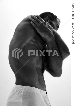 Close-up of man's side profile, showing his athletic body, arm muscles flexed as he stretches. Photo in monochrome filter. Close-up of man's side profile, showing his athletic body, arm muscles flexed as he stretches. Photo in monochrome filter. 118310508