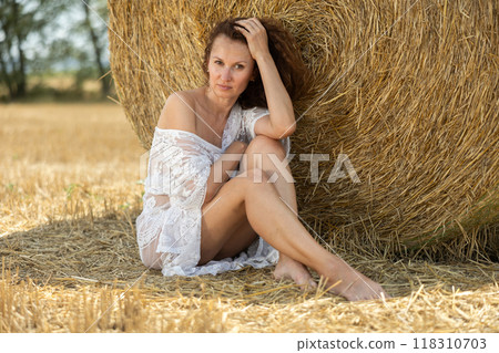 Woman in white negligee sitting by haystack Woman in white negligee sitting by haystack 118310703