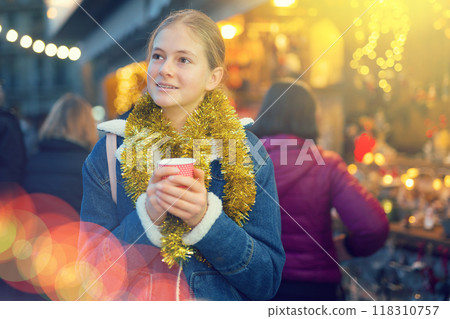 Teenagers girl holding hot cup of coffee in hands at street christmas fair Teenagers girl holding hot cup of coffee in hands at street christmas fair 118310757