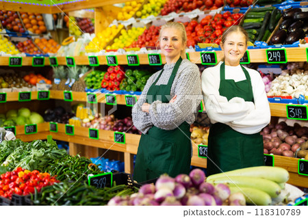Confident smiling saleswoman standing with trainee salesgirl in greengrocery store 118310789