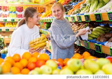 Mother and teenage daughter choosing fruits and vegetables in greengrocery Mother and teenage daughter choosing fruits and vegetables in greengrocery 118310801