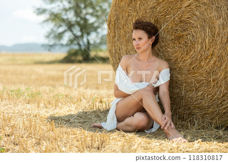 Woman with loose hair relaxing near hay bales on summer farm field 118310817