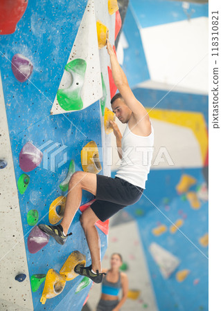 Sporty man in doing difficult wall climb in climbing gym without special climbing equipment 118310821
