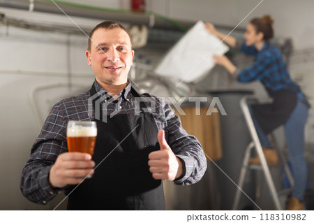 Happy brewer showing thumbs up while holding out glass of beer 118310982