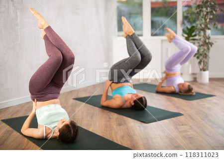 Diligent women practicing half shoulder stand pose of yoga in light fitness room Diligent women practicing half shoulder stand pose of yoga in light fitness room 118311023