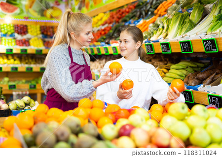 Saleswoman helping teenage girl to choose oranges in supermarket 118311024