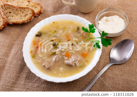 Popular dish of Russian cuisine is pickle soup with meat, cooked on basis of pickled cucumbers and pearl barley or rice, decorated with sprig of parsley 118311026