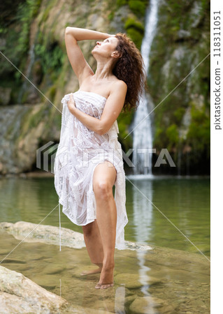 Woman in white negligee stands by waterfall 118311051