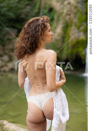 Rear view of seminude woman covering breasts with lace by waterfall 118311095