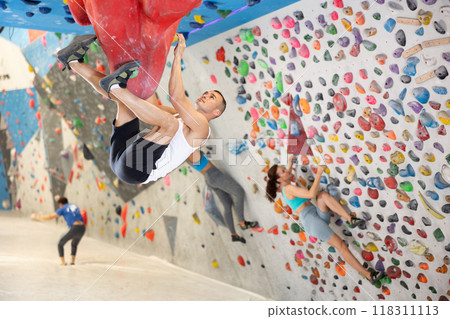 Young man and two women engaged in rock-climbing in indoor hangar 118311113