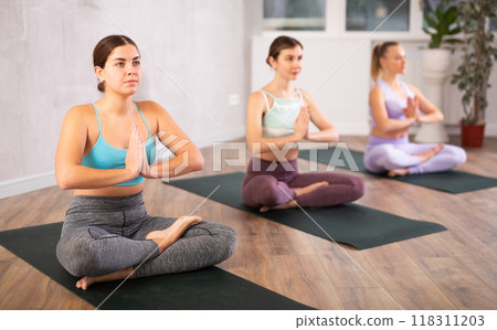 Diligent women practicing lotus pose of yoga in light fitness room Diligent women practicing lotus pose of yoga in light fitness room 118311203