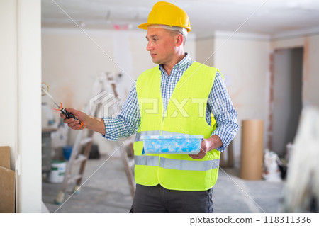 Portrait of positive man painter in a protective helmet and overal with paint roller 118311336