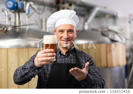 Satisfied professional brewer holding out glass with craft beer Satisfied professional brewer holding out glass with craft beer 118311438