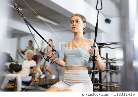 Active athlete young woman during exercises on crossover exercise machine with loops and weighting 118311439