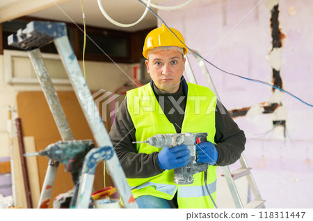 Repair man in yellow vest and helmet with drill in apartment 118311447