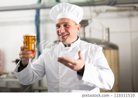 Satisfied professional brewer holding out glass with craft beer 118311510