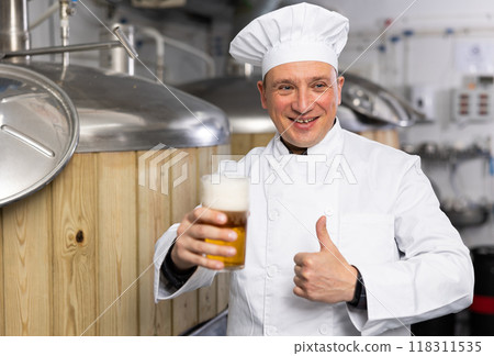 Successful brewmaster holding glass of amber ale and giving thumbs up 118311535