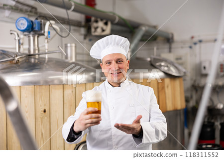 Successful brewmaster holding glass of foamy pale ale Successful brewmaster holding glass of foamy pale ale 118311552