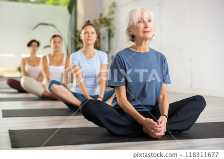 Sporty mature aged european woman practicing yoga in lotus position during group training in yoga class Sporty mature aged european woman practicing yoga in lotus position during group training in yoga class 118311677