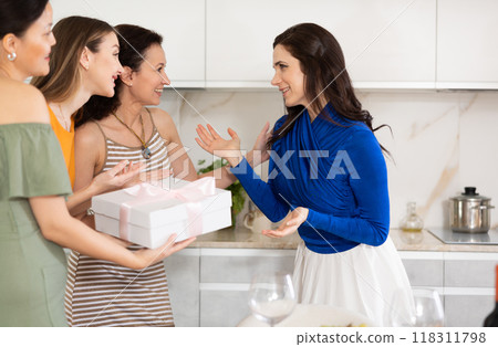 Excited woman greeting besties bringing gift for house party Excited woman greeting besties bringing gift for house party 118311798