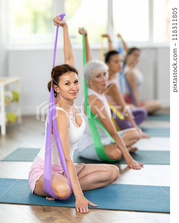 Women are doing stretching exercise with resistance bands. Teamwork, good mood and healthy lifestyle concept in gym 118311805