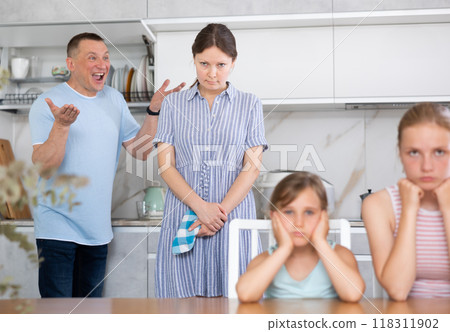 Husband yells at wife while children put their hands over their ears Husband yells at wife while children put their hands over their ears 118311902